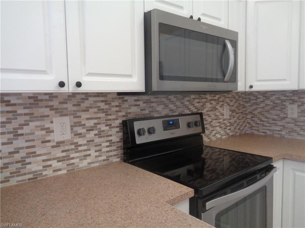 Kitchen with stainless steel microwave, stove & oven, backsplash, white cabinetry, and light countertops