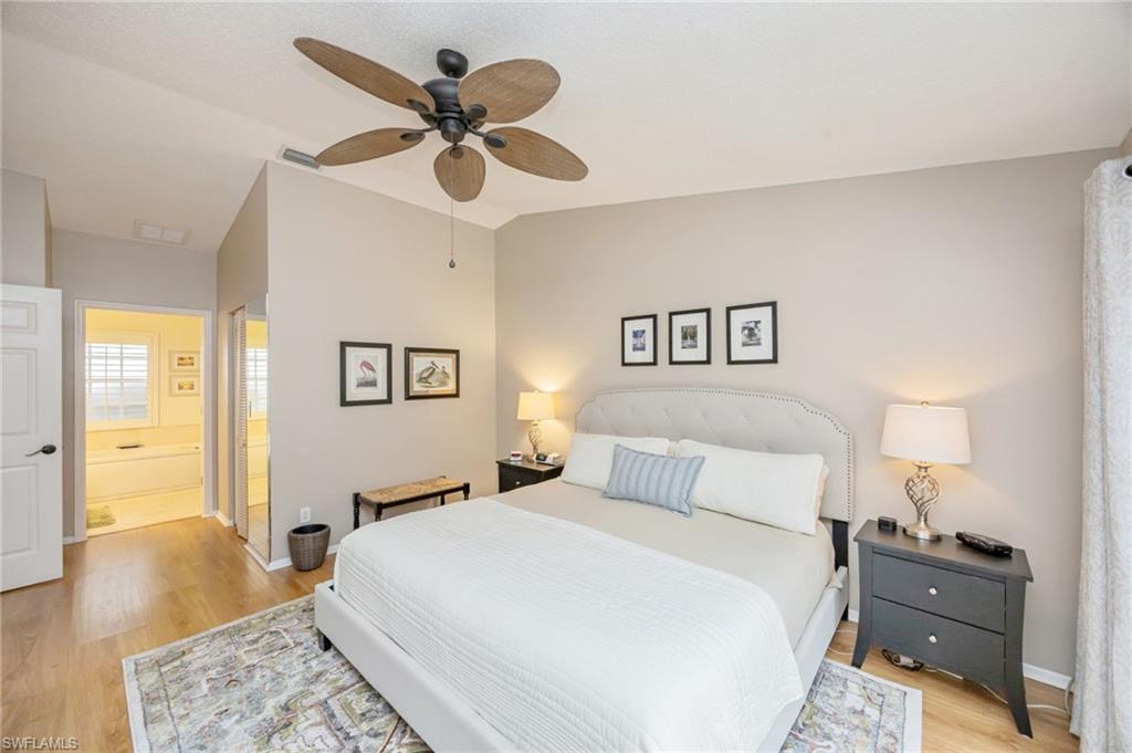 Bedroom with king sized bed, light wood-type flooring, lofted ceiling, a ceiling fan, and connected bathroom