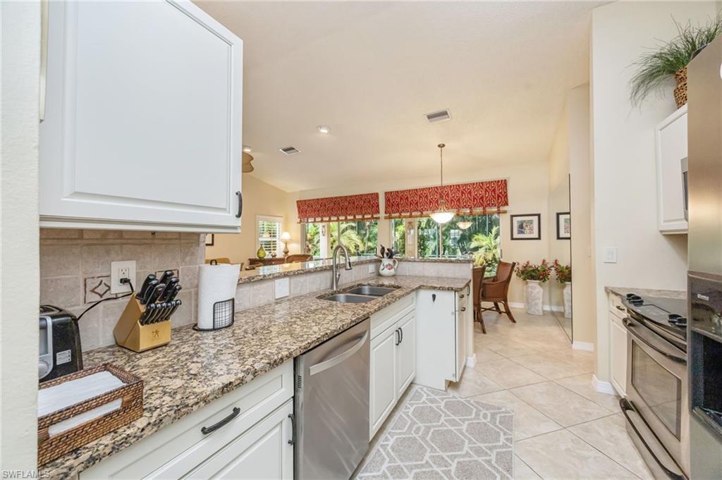Kitchen with white cabinets, stainless steel appliances, light stone countertops, and a peninsula