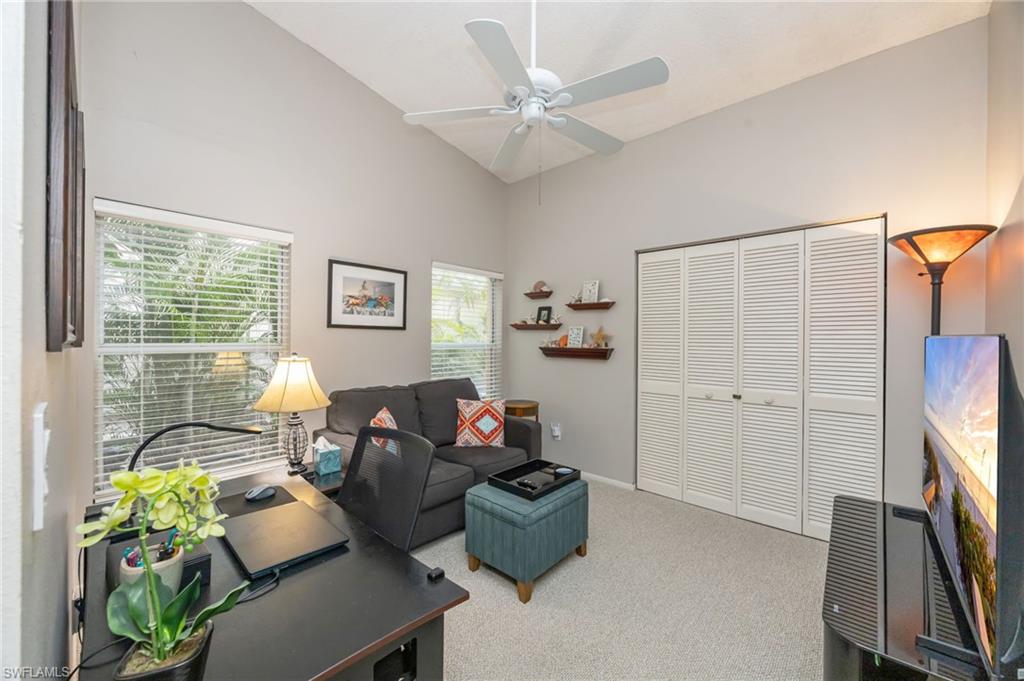 Carpeted living area with a desk, ceiling fan, and high vaulted ceiling, couch can be made into a single sized bed