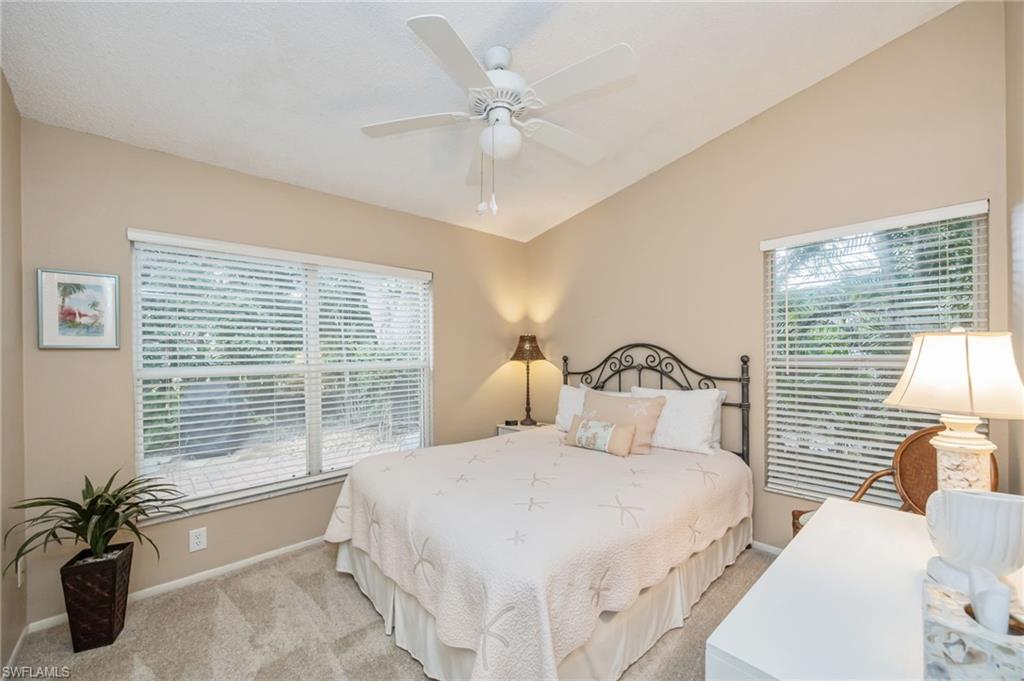 Carpeted bedroom with queen sized bed, featuring ceiling fan and vaulted ceiling