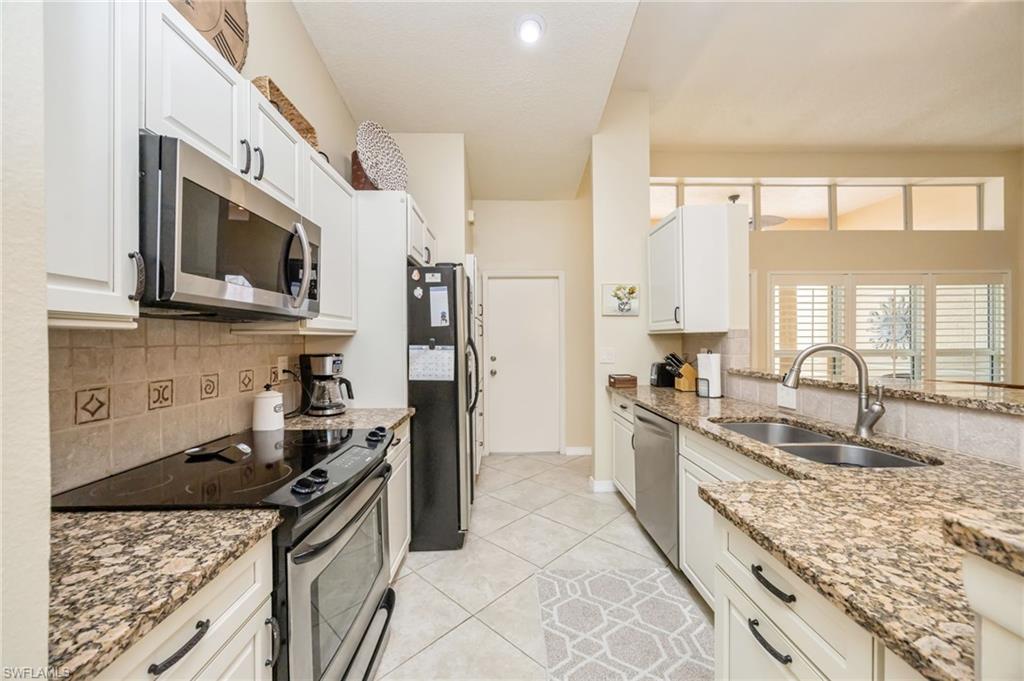 Kitchen with stainless steel appliances, light stone countertops, decorative backsplash, light tile patterned floors, and white cabinets