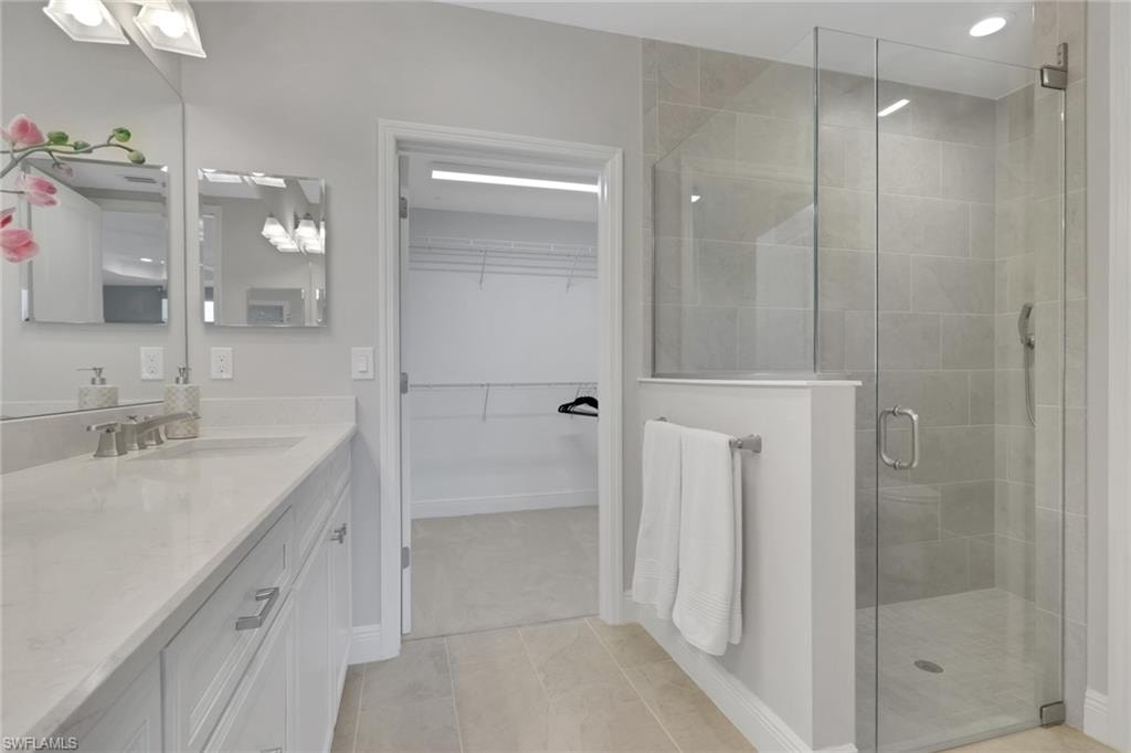 Full bath with a walk in closet, vanity, a stall shower, and light tile patterned floors