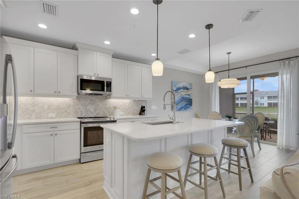 Kitchen with stainless steel appliances, light wood-type flooring, an island with sink, a kitchen breakfast bar, and white cabinets