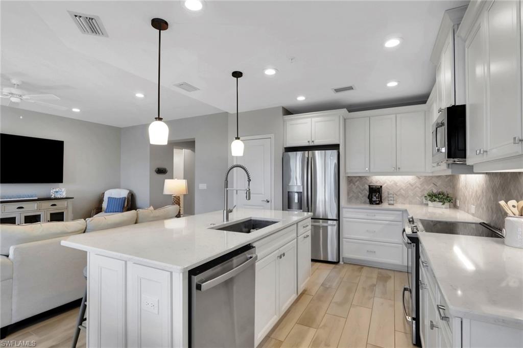 Kitchen featuring open floor plan, a breakfast bar, stainless steel appliances, wood tiled floors, and white cabinets
