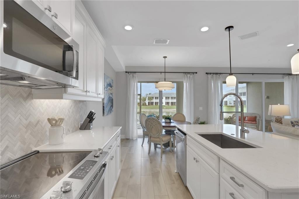 Kitchen featuring white cabinets, stainless steel appliances, light stone countertops, hanging light fixtures, and a center island with sink