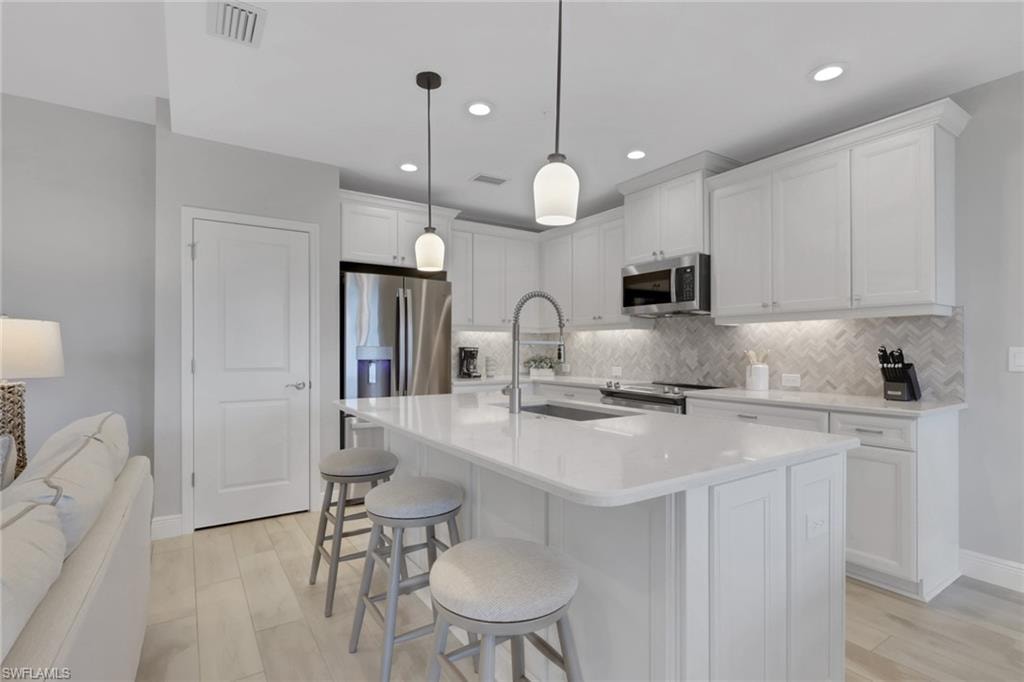 Kitchen with white cabinets, a kitchen breakfast bar, a center island with sink, stainless steel appliances, and light stone counters