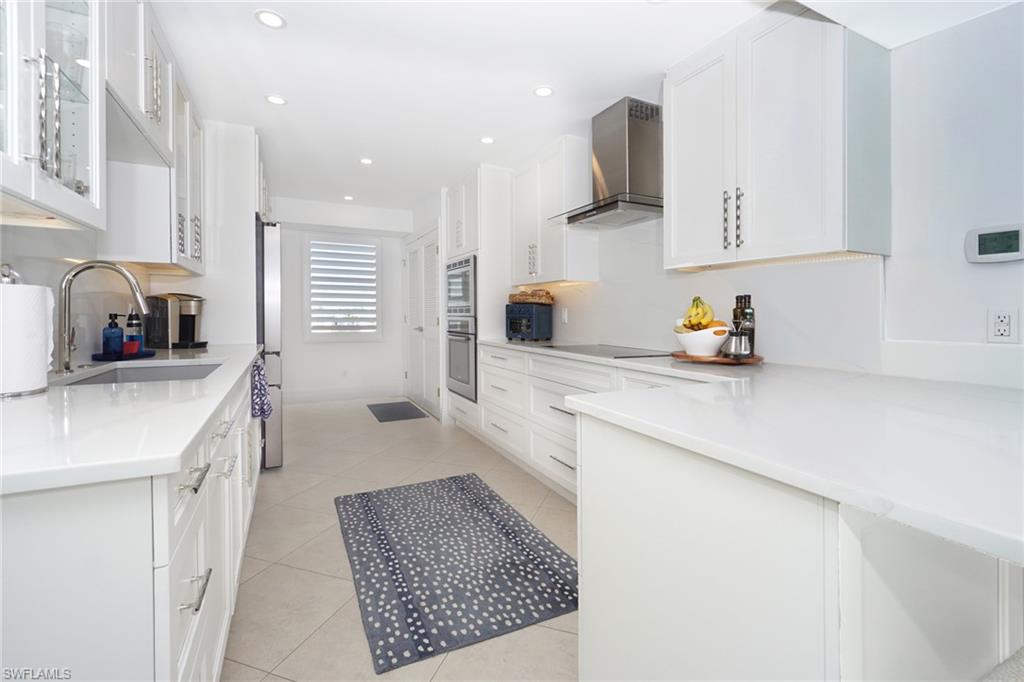 Kitchen featuring white cabinets, glass insert cabinets, wall chimney exhaust hood, light stone counters, and light tile patterned floors