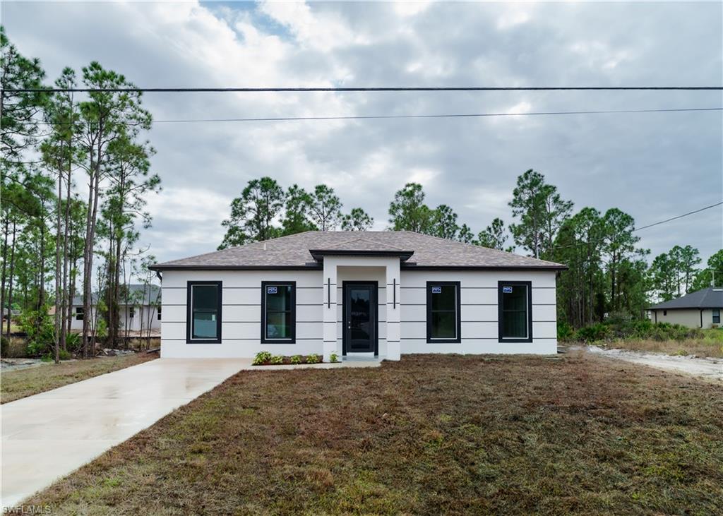 View of front of house featuring a front yard, roof with shingles, stucco siding, and concrete driveway