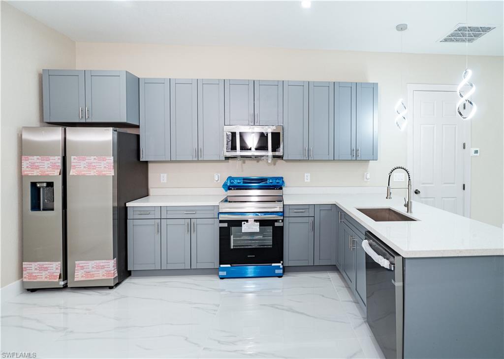 Kitchen featuring a peninsula, stainless steel appliances, decorative light fixtures, light marble finish floors, and gray cabinetry