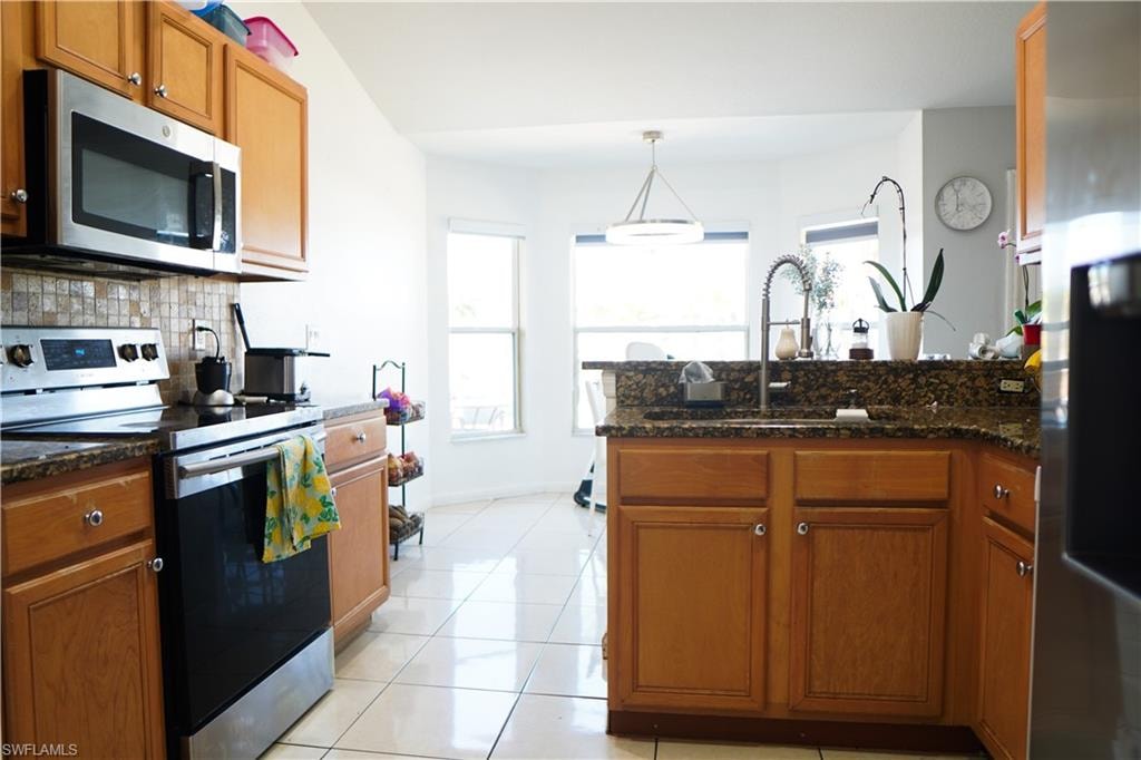 Kitchen featuring stainless steel appliances, wood finish cabinets, a peninsula, decorative light fixtures, and light tile patterned floors