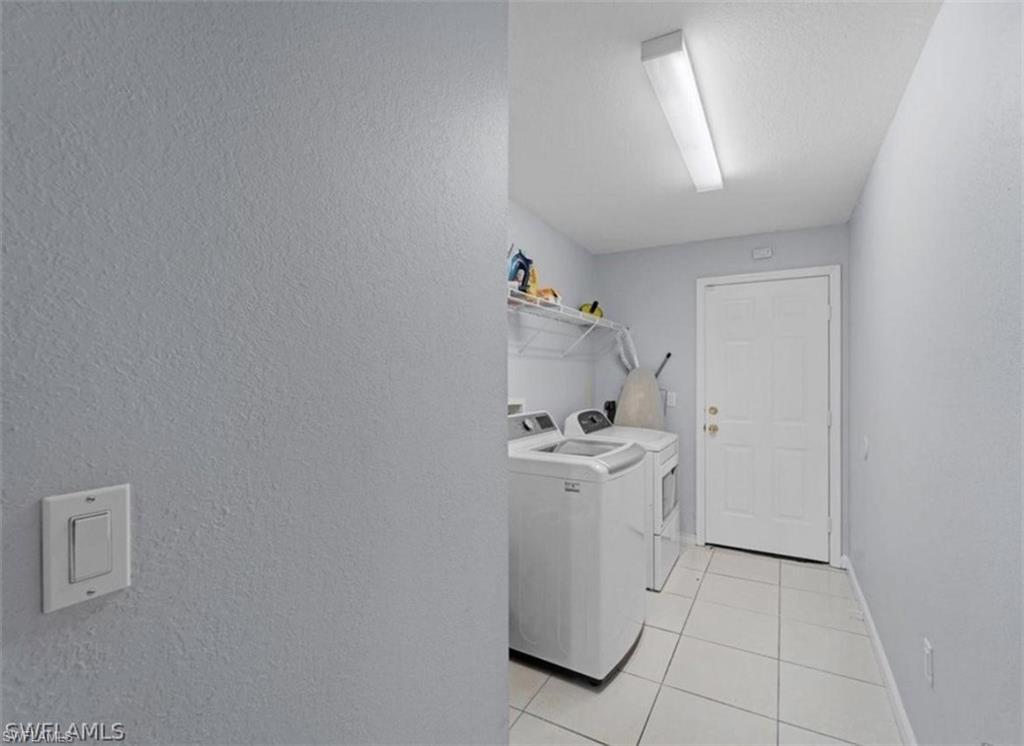 Laundry room featuring a textured wall, washer and dryer, and light tile patterned floors