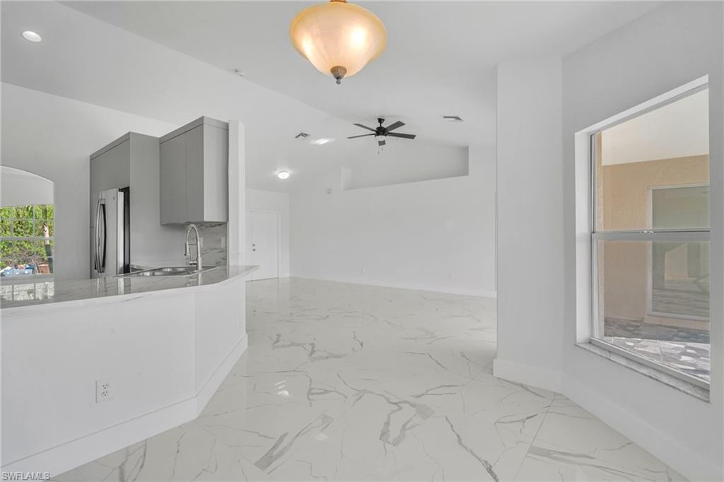 Kitchen featuring gray cabinetry, light stone countertops, freestanding refrigerator, lofted ceiling, and decorative light fixtures