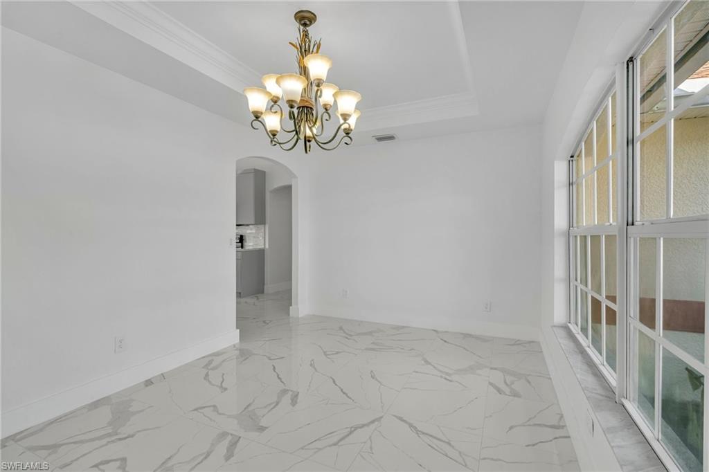 Unfurnished room featuring a chandelier, a tray ceiling, arched walkways, light marble finish floors, and crown molding