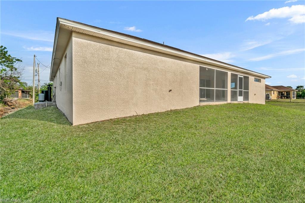 Rear view of property featuring stucco siding, a sunroom, and a lawn