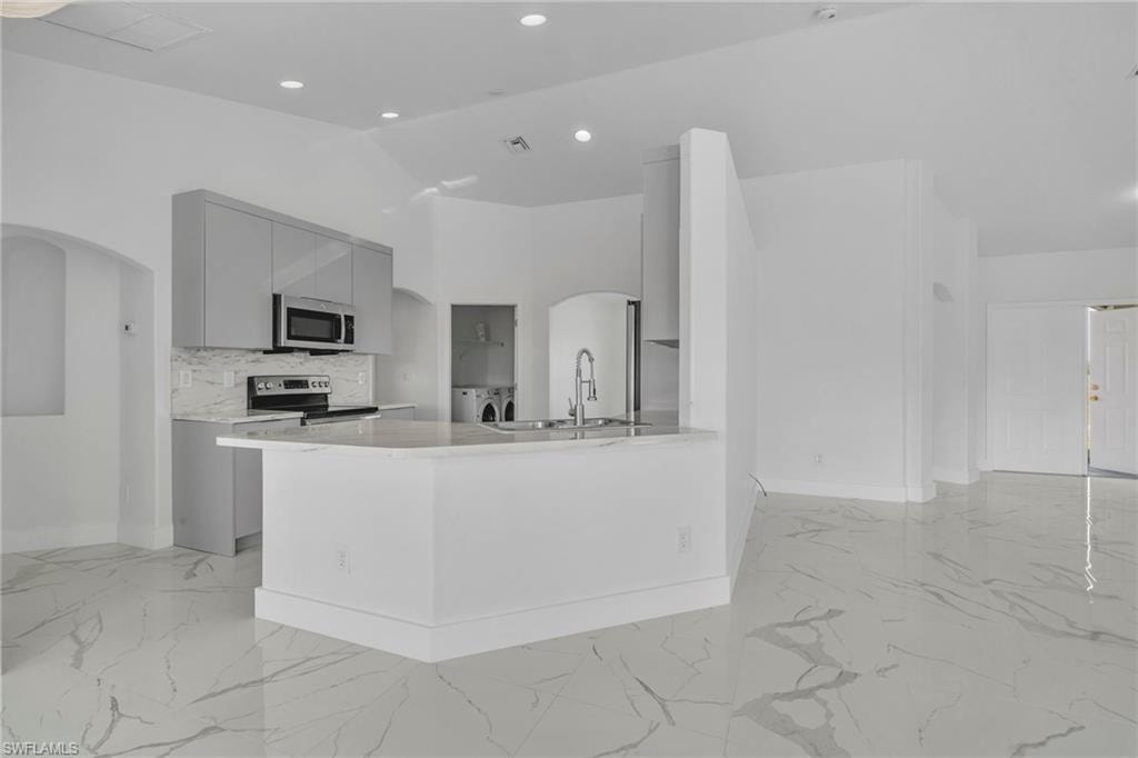 Kitchen with gray cabinetry, arched walkways, modern cabinets, a peninsula, and vaulted ceiling