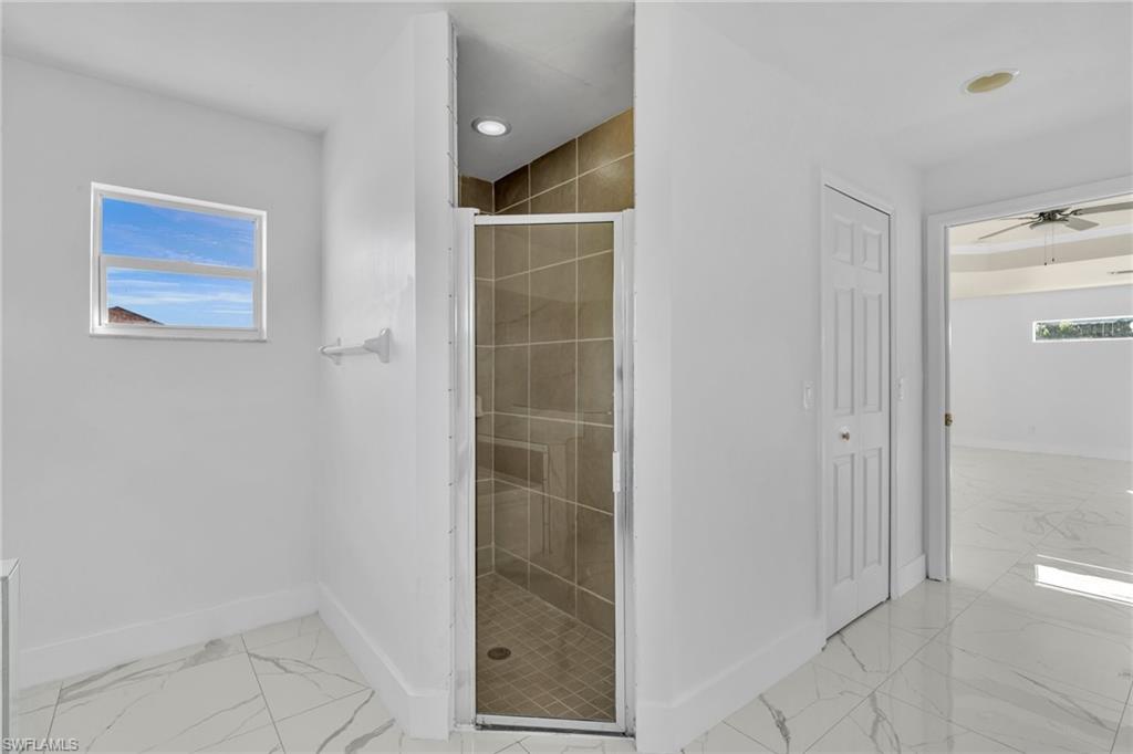 Full bathroom featuring a stall shower, ceiling fan, and light marble finish floors