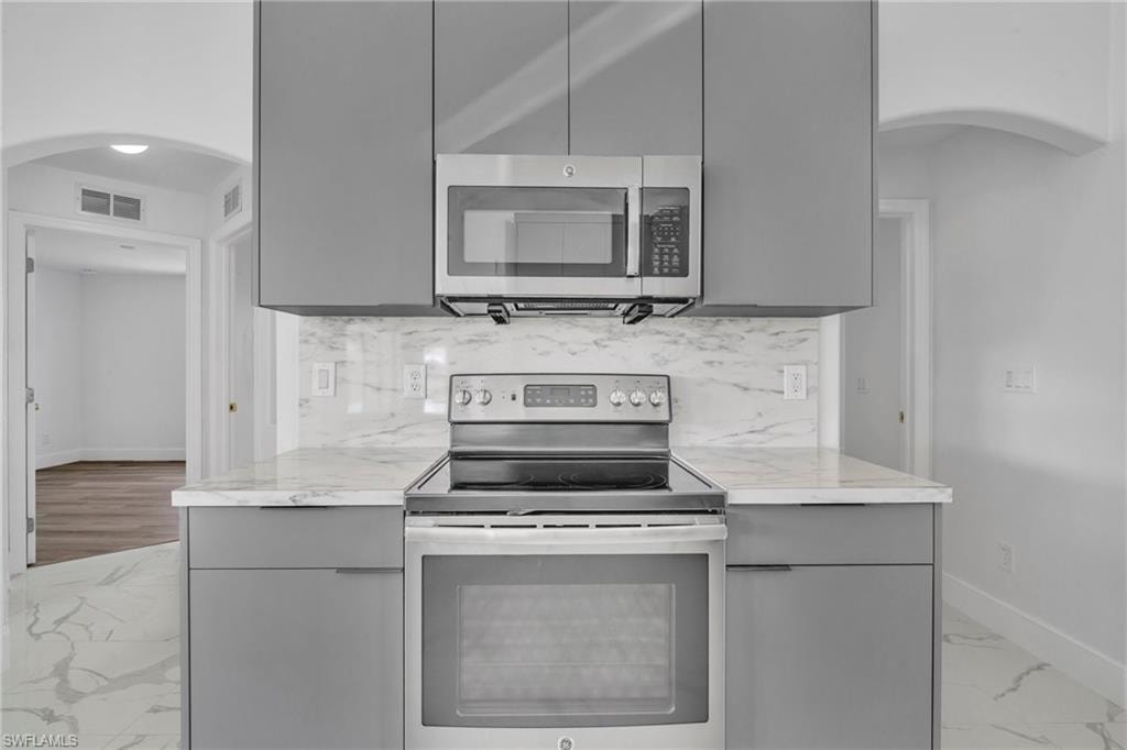 Kitchen featuring arched walkways, light marble finish floors, appliances with stainless steel finishes, and gray cabinets