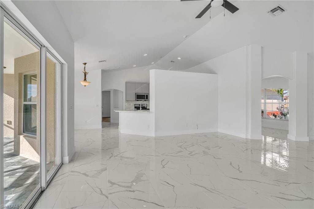 Spare room featuring arched walkways, vaulted ceiling, light marble finish flooring, and ceiling fan