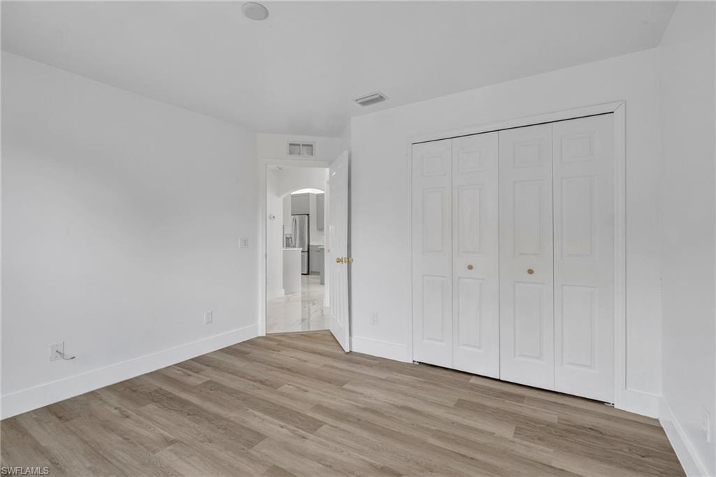 Unfurnished bedroom featuring arched walkways, light wood-type flooring, a closet, and freestanding refrigerator