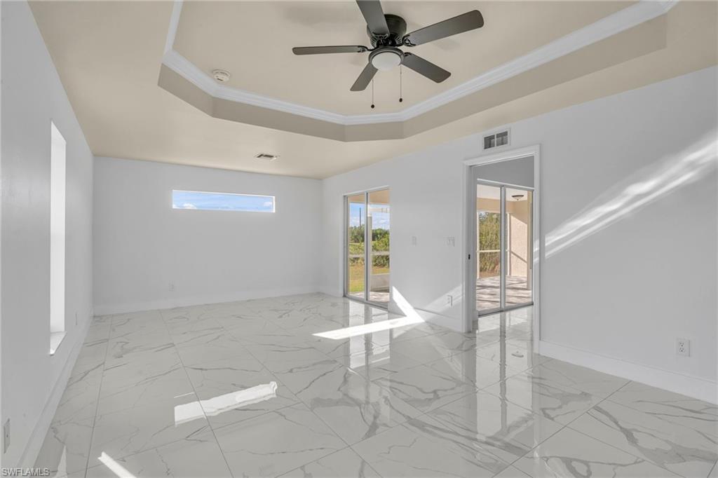 Unfurnished room with a tray ceiling, ornamental molding, light marble finish floors, and a ceiling fan