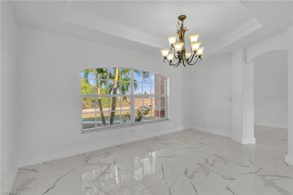 Spare room featuring a chandelier, a raised ceiling, ornamental molding, arched walkways, and light marble finish floors