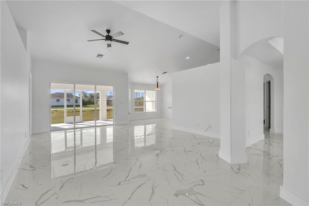 Spare room with light marble finish flooring, arched walkways, ceiling fan, and a towering ceiling