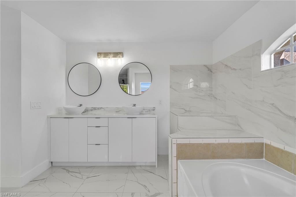 Bathroom featuring double vanity, a garden tub, and light marble finish flooring