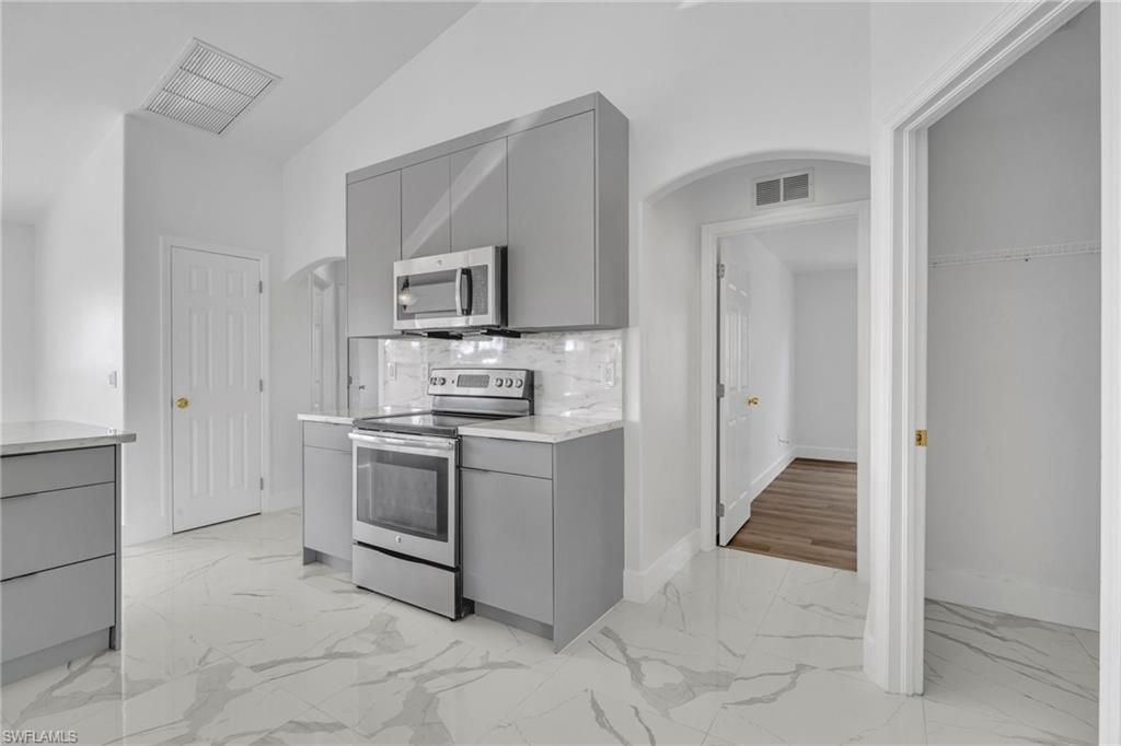 Kitchen with gray cabinets, arched walkways, light marble finish floors, and lofted ceiling