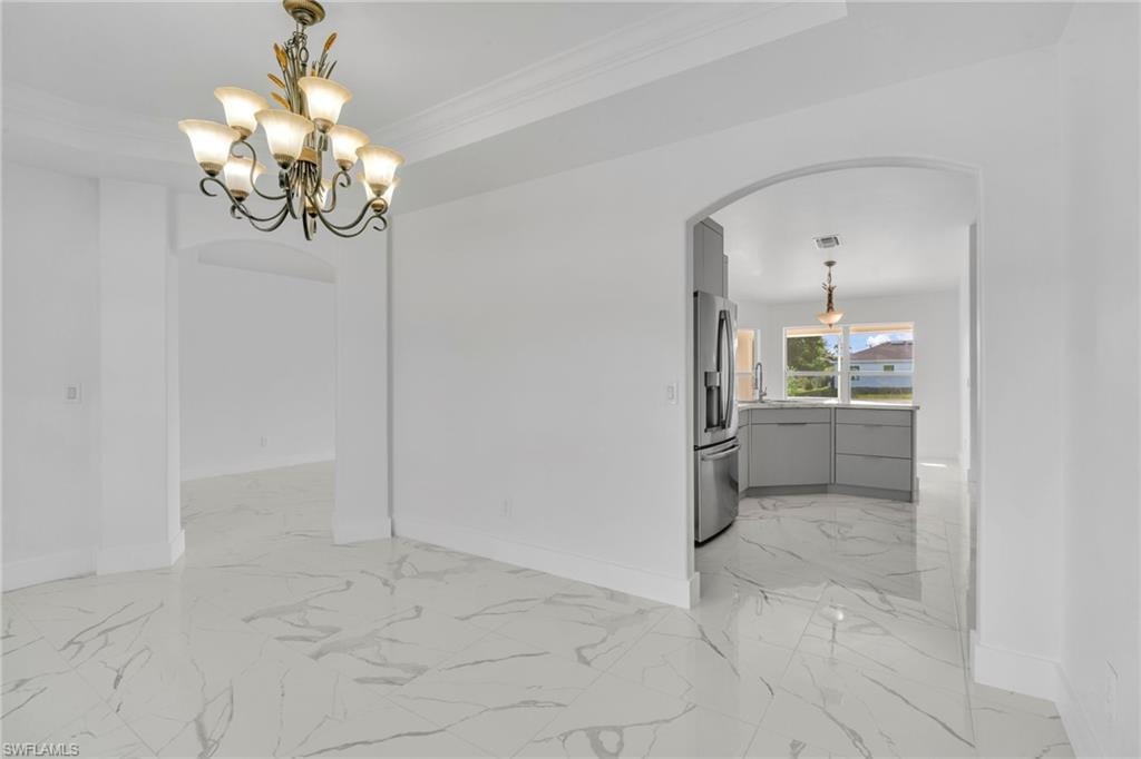 Unfurnished dining area featuring arched walkways, light marble finish floors, ornamental molding, and a chandelier