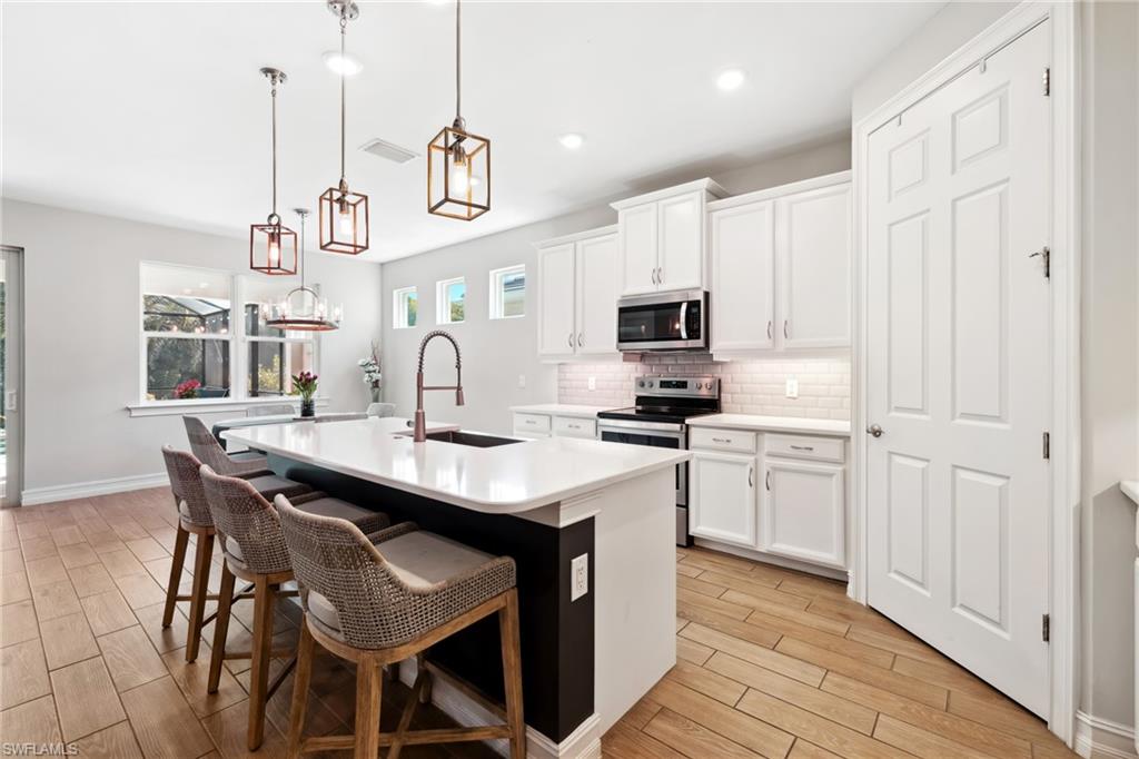 Kitchen with a kitchen island with sink, appliances with stainless steel finishes, a breakfast bar, decorative light fixtures, and wood tiled floors