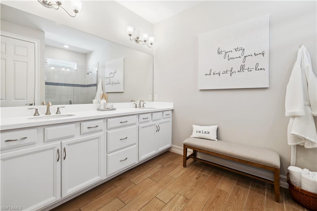 Bathroom featuring a stall shower, double vanity, and light wood-style flooring