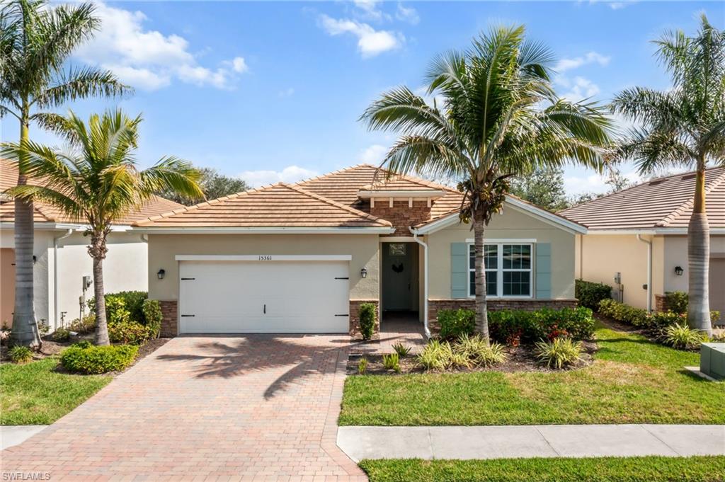 View of front of property with stucco siding, decorative driveway, an attached garage, a front yard, and stone siding