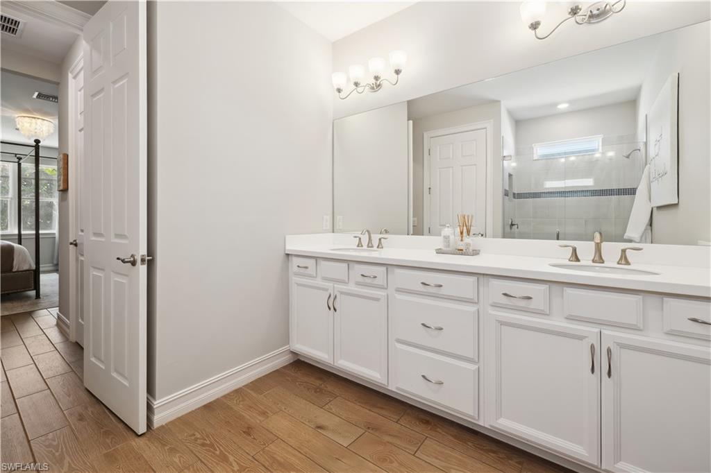 Ensuite bathroom featuring double vanity, light wood-type flooring, and a stall shower
