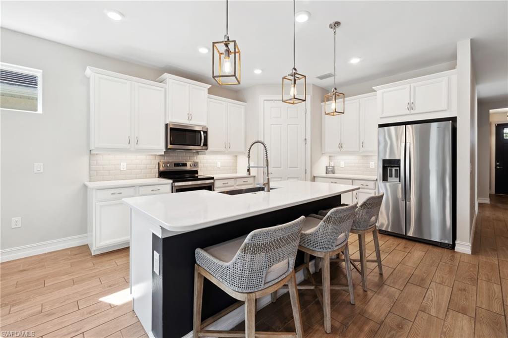 Kitchen with wood tiled floors, appliances with stainless steel finishes, white cabinets, a kitchen breakfast bar, and recessed lighting
