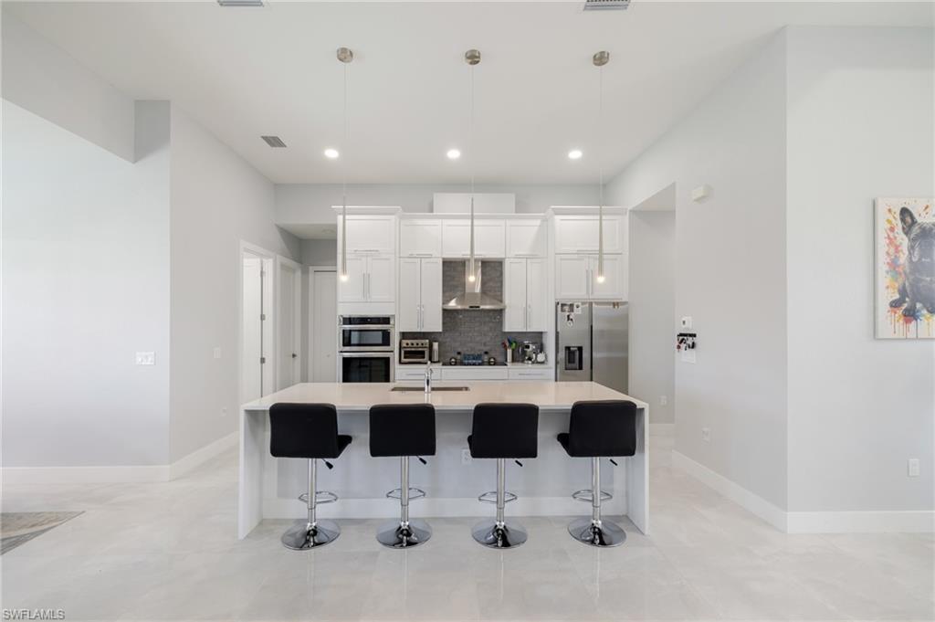Kitchen featuring a breakfast bar, wall chimney range hood, white cabinetry, appliances with stainless steel finishes, and a center island with sink