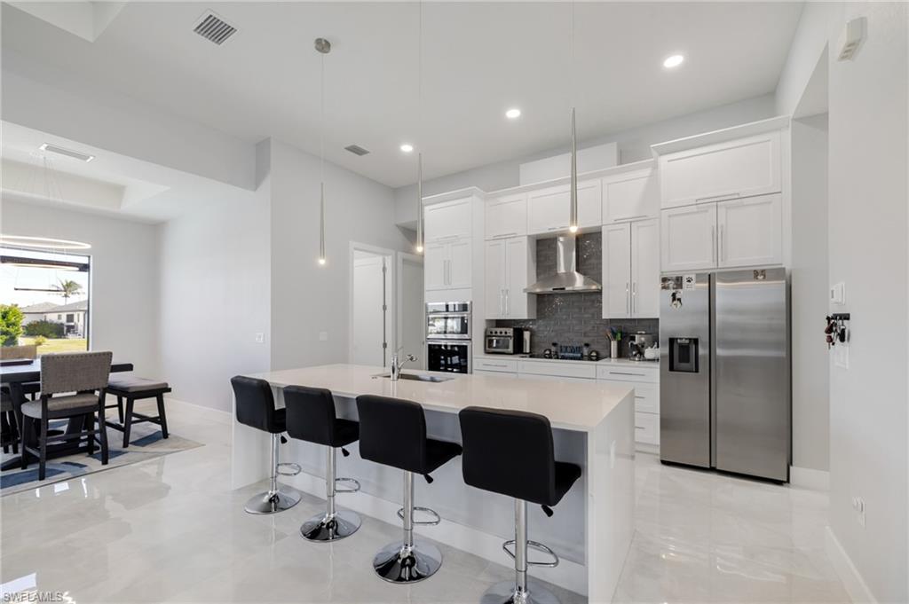Kitchen with appliances with stainless steel finishes, a breakfast bar area, hanging light fixtures, a kitchen island with sink, and recessed lighting