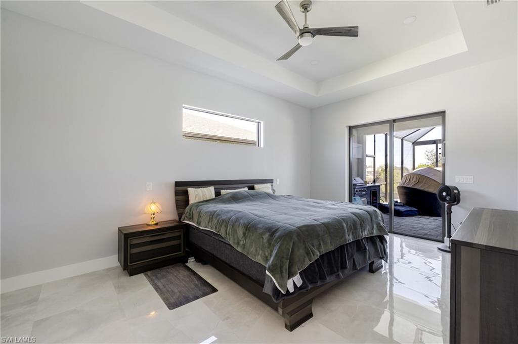 Bedroom with multiple windows, access to exterior, ceiling fan, and a tray ceiling