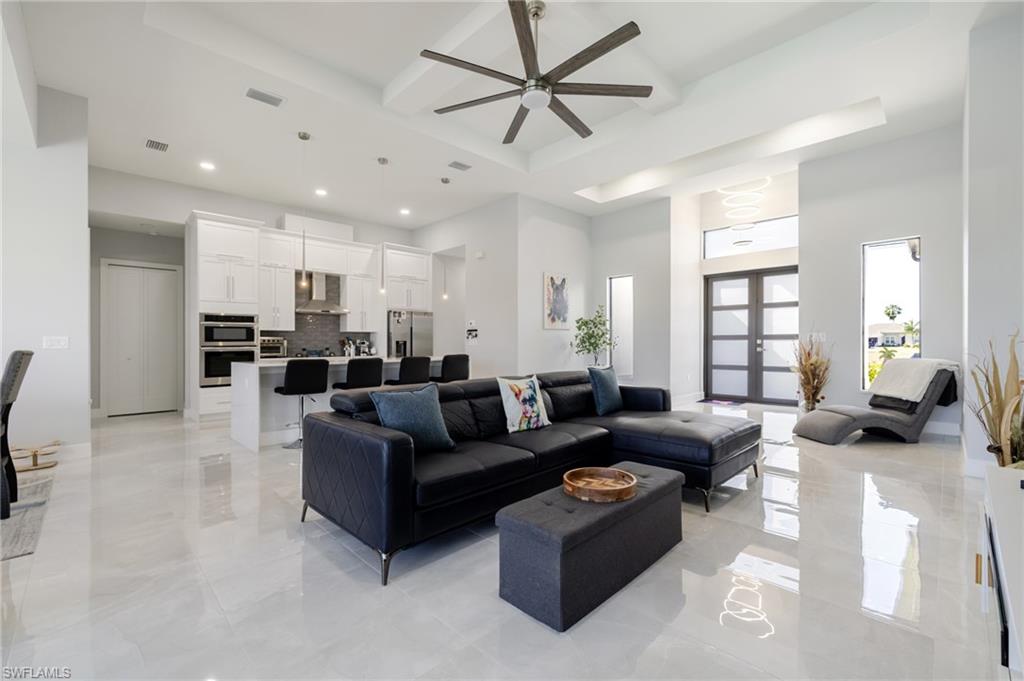 Living room featuring a raised ceiling, a ceiling fan, a high ceiling, coffered ceiling, and recessed lighting