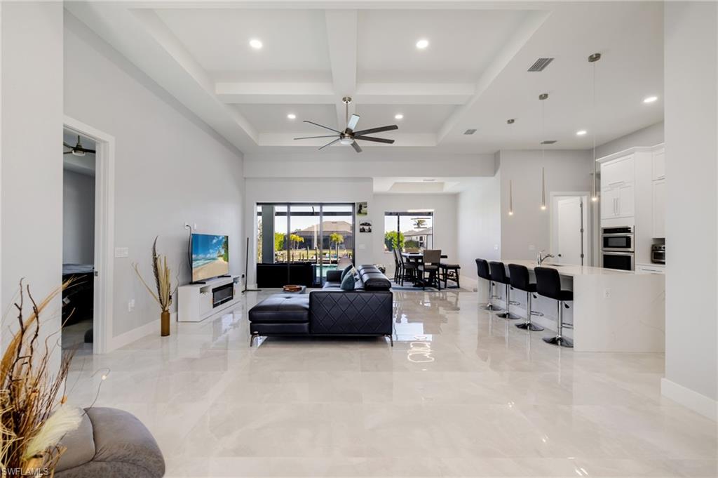 Living room with coffered ceiling, beamed ceiling, a ceiling fan, a high ceiling, and recessed lighting