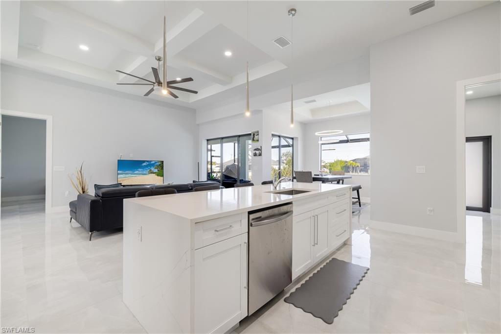 Kitchen with coffered ceiling, open floor plan, white cabinetry, light stone counters, and stainless steel dishwasher