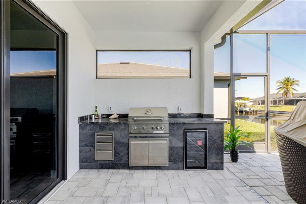 View of patio featuring exterior kitchen, a sunroom, beverage cooler, a water view, and a lanai