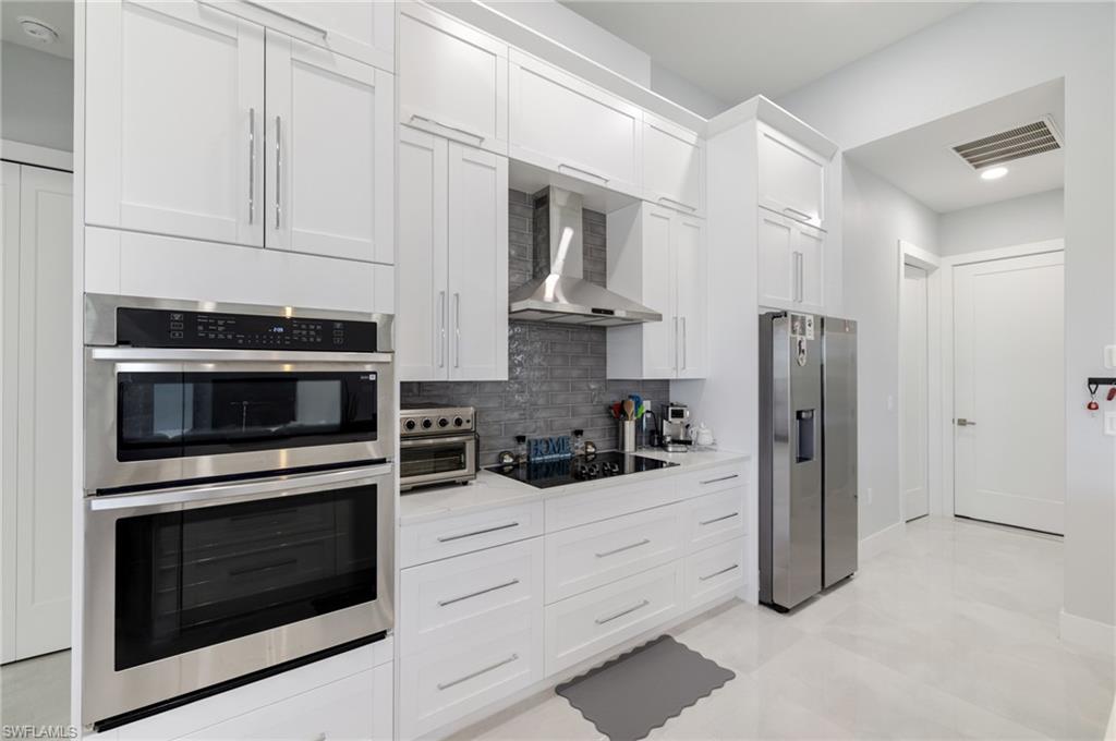 Kitchen featuring appliances with stainless steel finishes, wall chimney exhaust hood, white cabinetry, decorative backsplash, and light stone counters