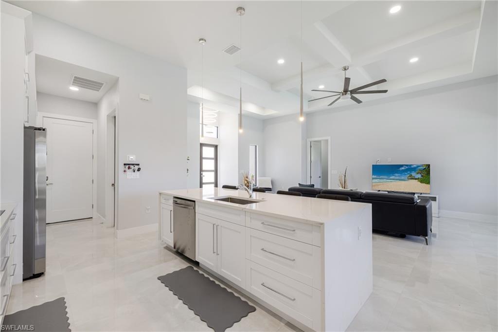 Kitchen with white cabinetry, coffered ceiling, hanging light fixtures, a kitchen island with sink, and light stone counters