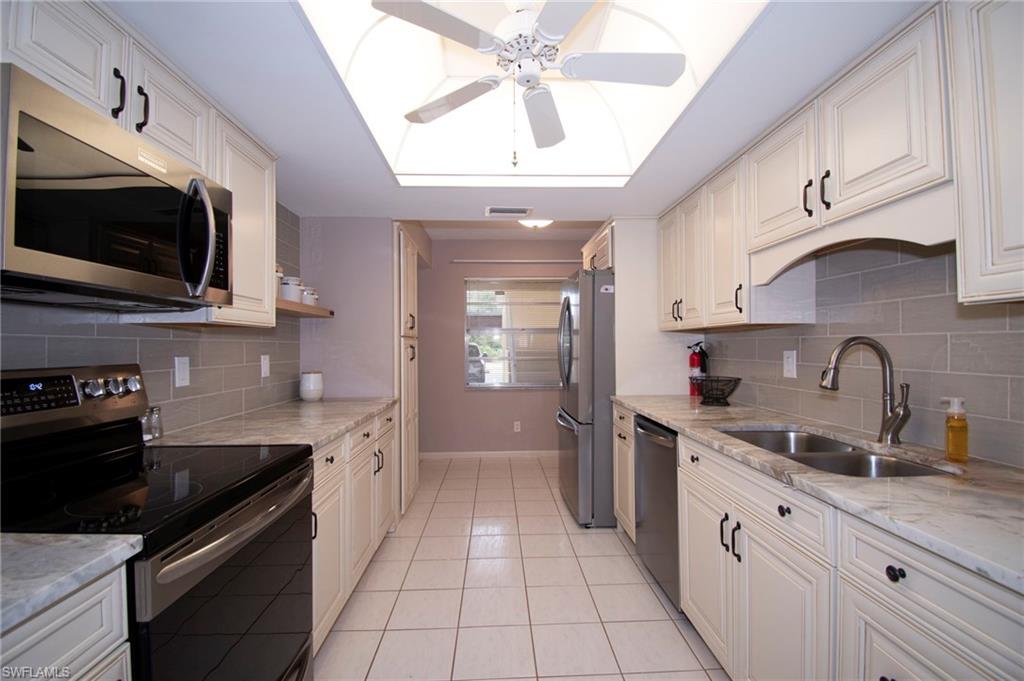 Kitchen with appliances with stainless steel finishes, light stone countertops, white cabinets, and a ceiling fan