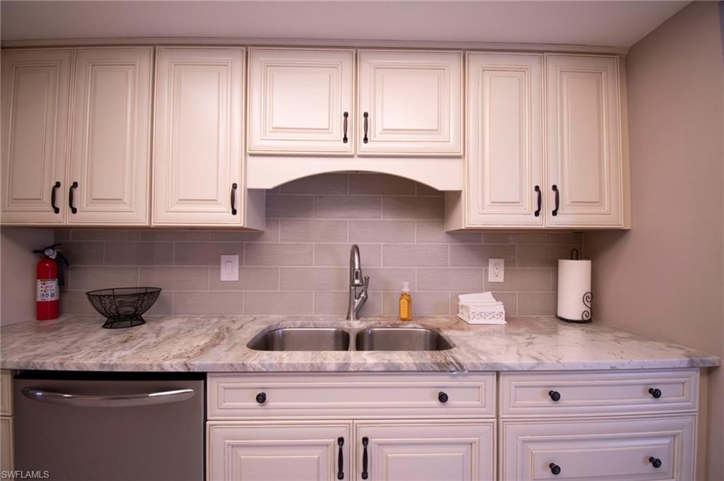 Kitchen with stainless steel dishwasher, light stone countertops, white cabinets, and tasteful backsplash