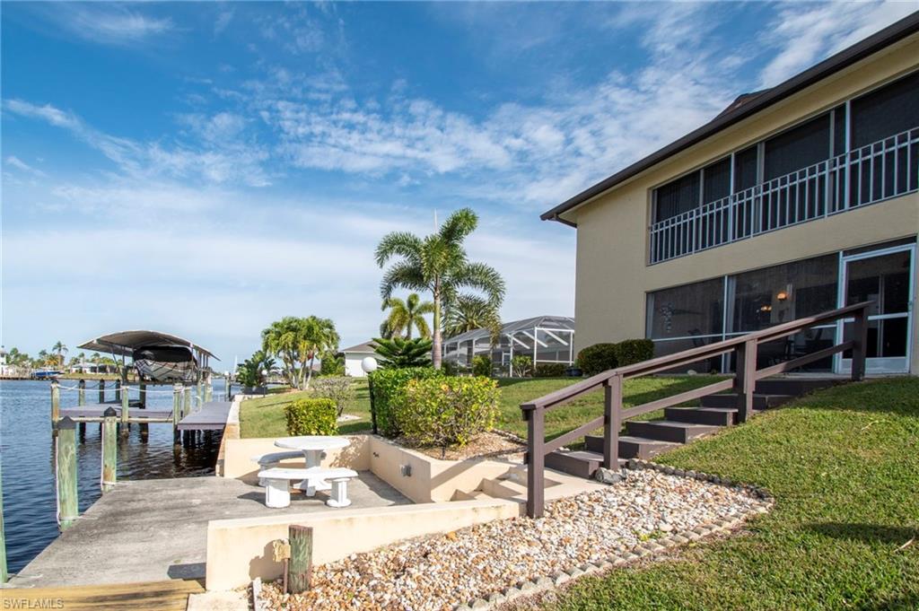 View of green lawn featuring a boat dock, a water view, boat lift, a sunroom, and a balcony