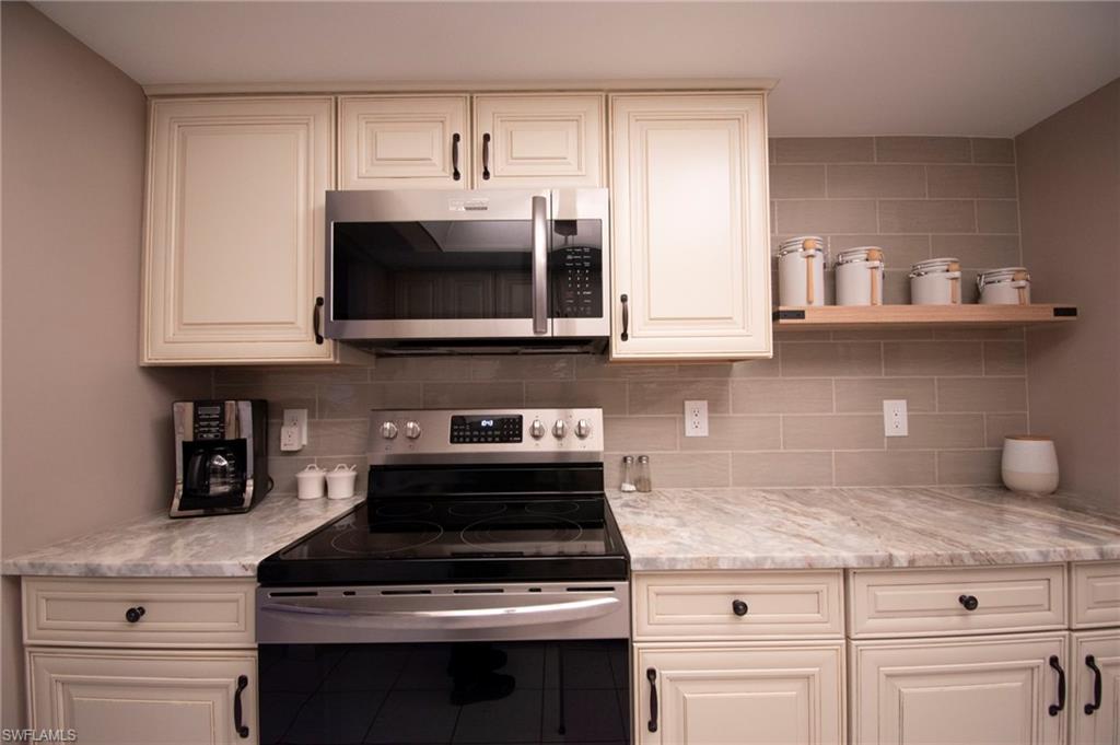 Kitchen with appliances with stainless steel finishes, backsplash, open shelves, and light stone countertops