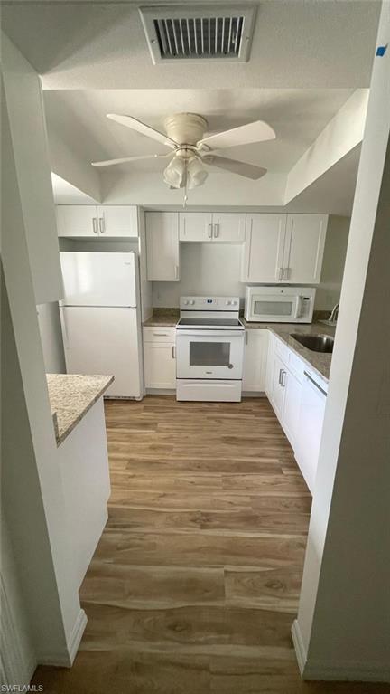 Kitchen with white cabinets, white appliances, light wood-style flooring