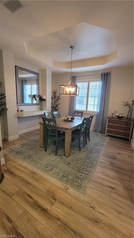 Dining area with a tray ceiling, plenty of natural light, light wood-style flooring, and suspended lighting